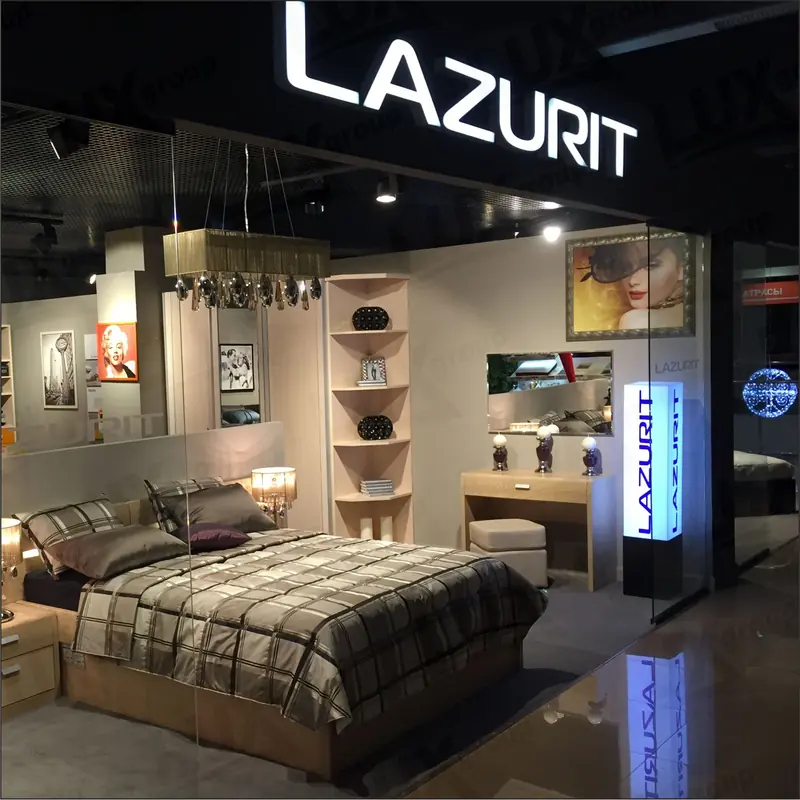 Мебельный стенд LAZURIT с кроватью, тумбами, зеркалом, полками, светильниками и световыми вывесками в открытом интерьере.
