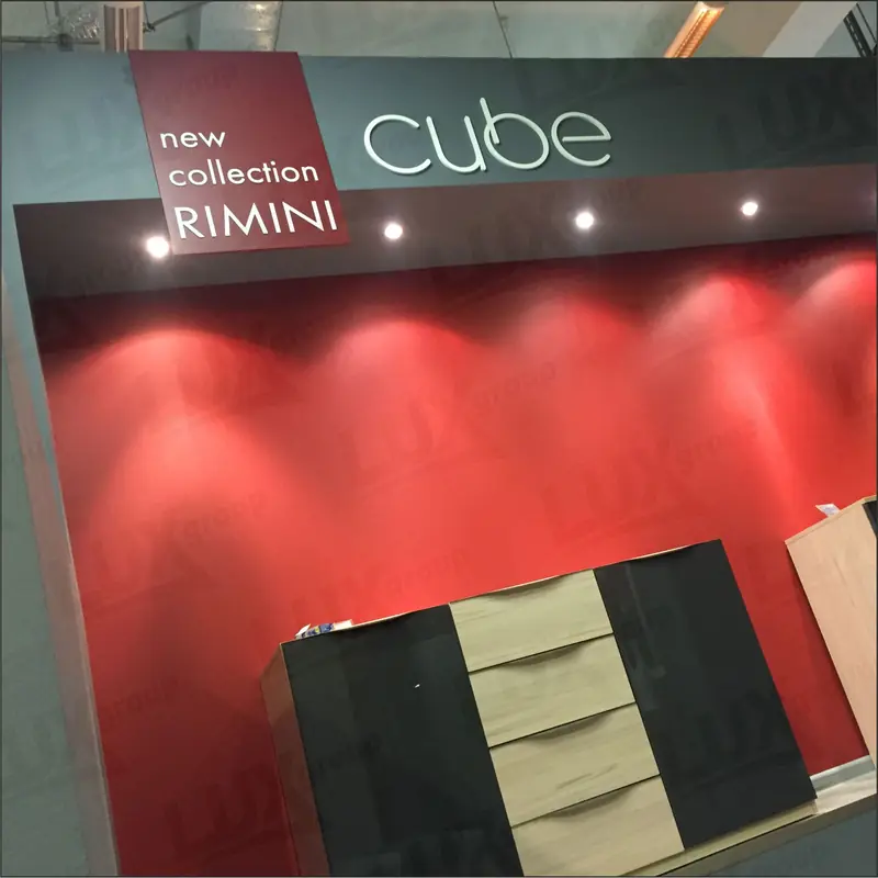 Выставочная мебельная зона cube с красной стеной, точечным освещением и панелью с надписью «new collection RIMINI».