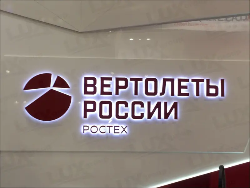 Объёмная вывеска с контражурной подсветкой: бордовые буквы «ВЕРТОЛЕТЫ РОССИИ», знак и надпись «РОСТЕХ» на белой стене.